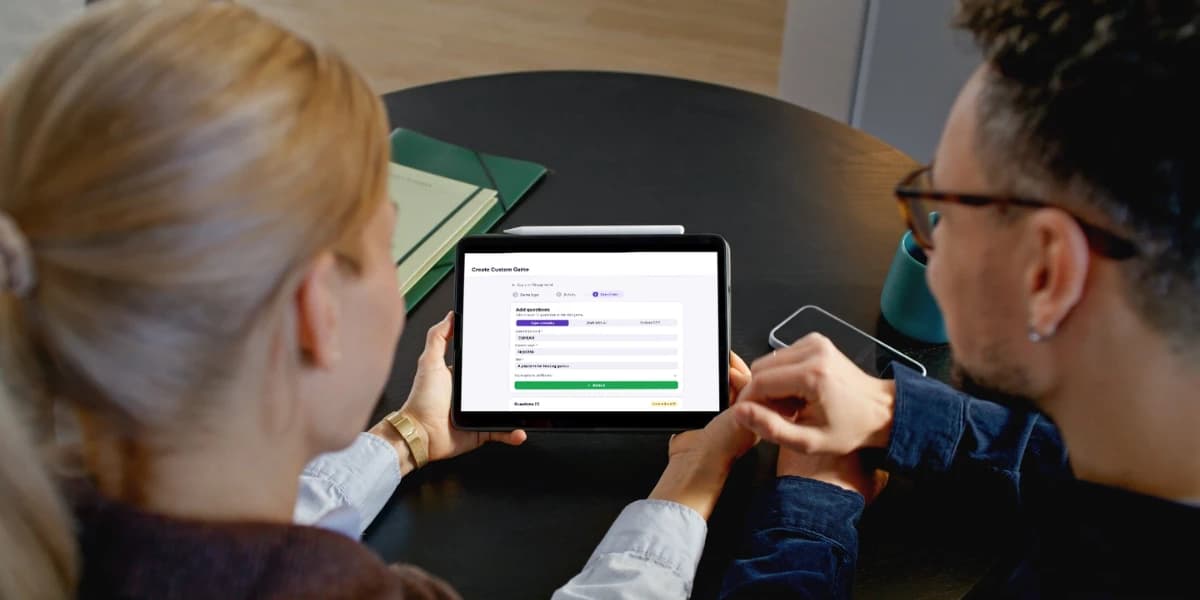 Two colleagues at a table looking at the Neegma Create Custom Game screen on a tablet