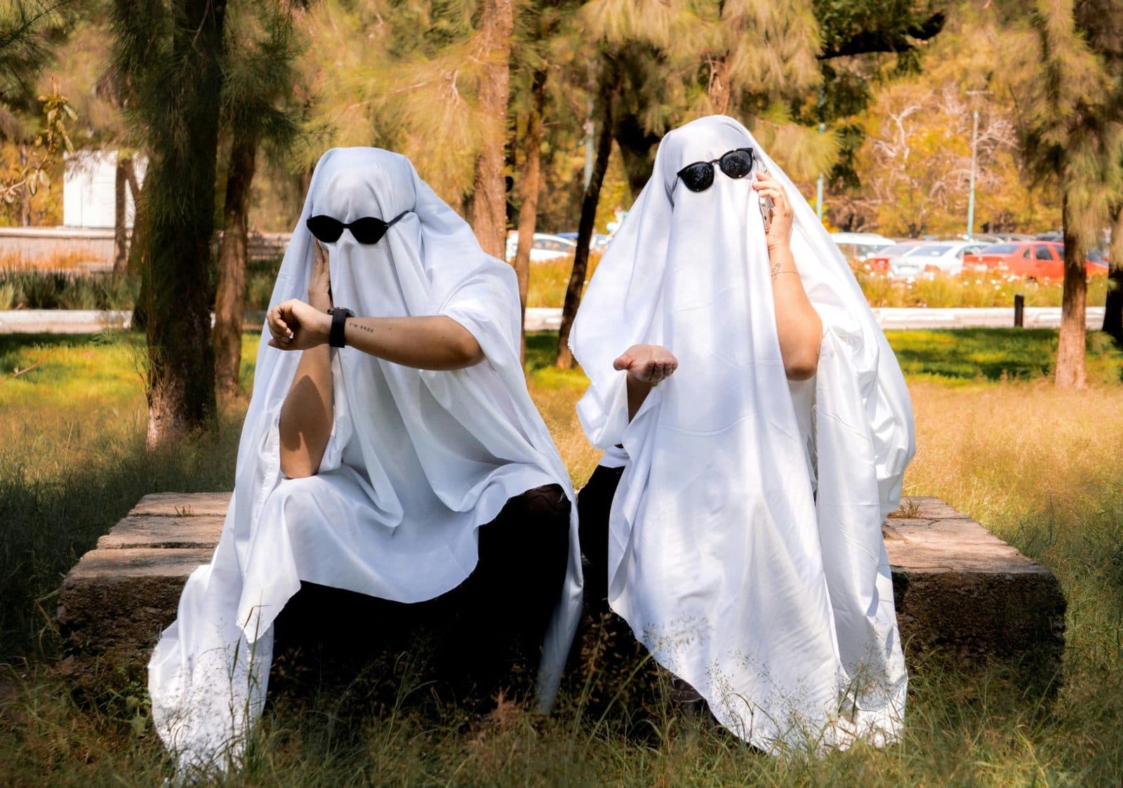 Two people dressed as ghosts sitting outside, ready for a Halloween party
