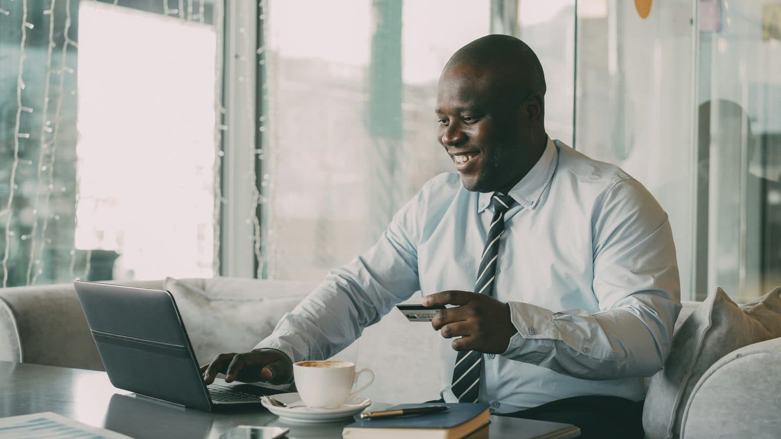 A man holding a credit card while using a laptop with a coffee, paying for something online